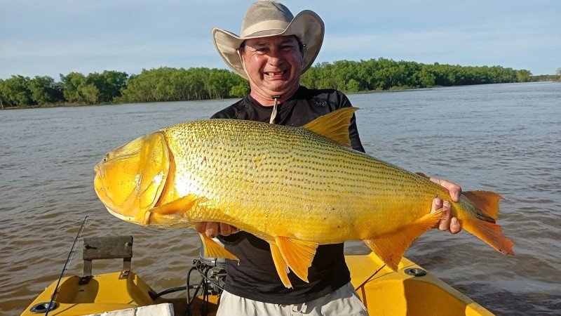 Pescador con sombrero sostiene un dorado en la lancha, Esquina, Corrientes